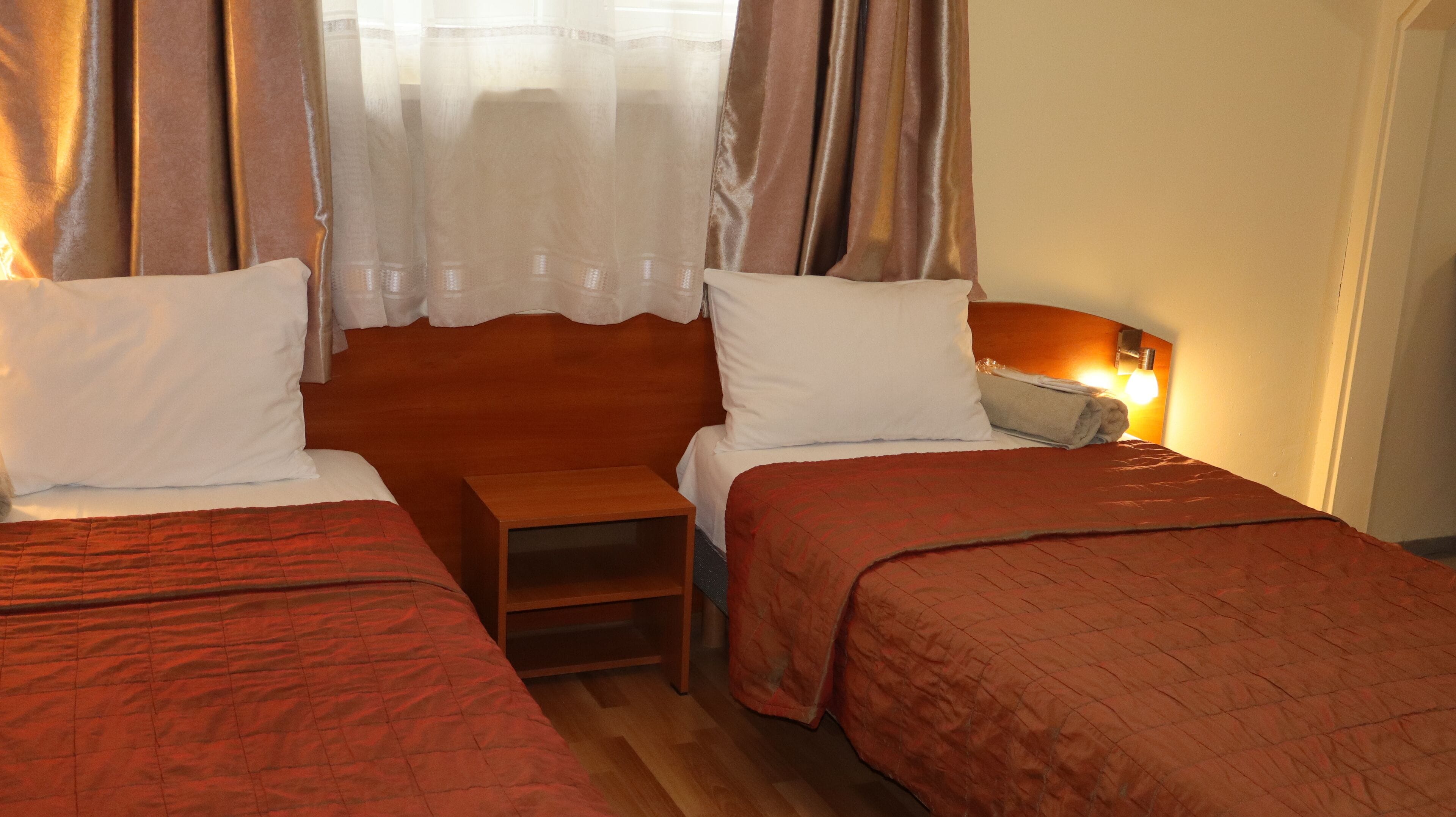 A hotel room with two beds, a nightstand, and a lamp.