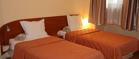 Una habitación de hotel con dos camas individuales, cada una con cabecero de madera, sábanas blancas y colcha acolchada naranja. Hay dos mesitas de noche con lámparas, y la habitación tiene una paleta de colores cálida y neutra.