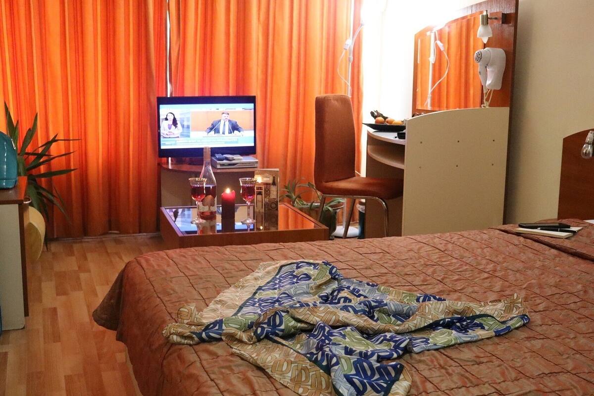 A hotel room with a bed, a desk with a computer, a chair, a television, and a suitcase.