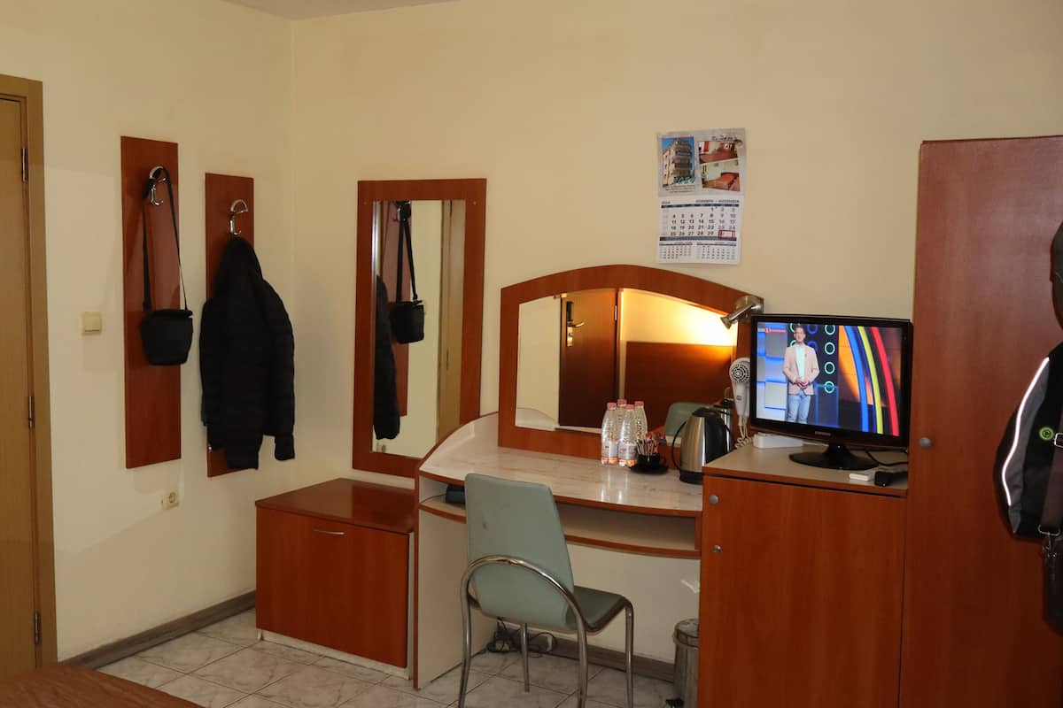 A hotel room with a wooden desk, a chair, a television, a mirror, and a door.