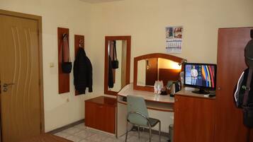 A hotel room with a wooden desk, a chair, a television, a mirror, and a door.