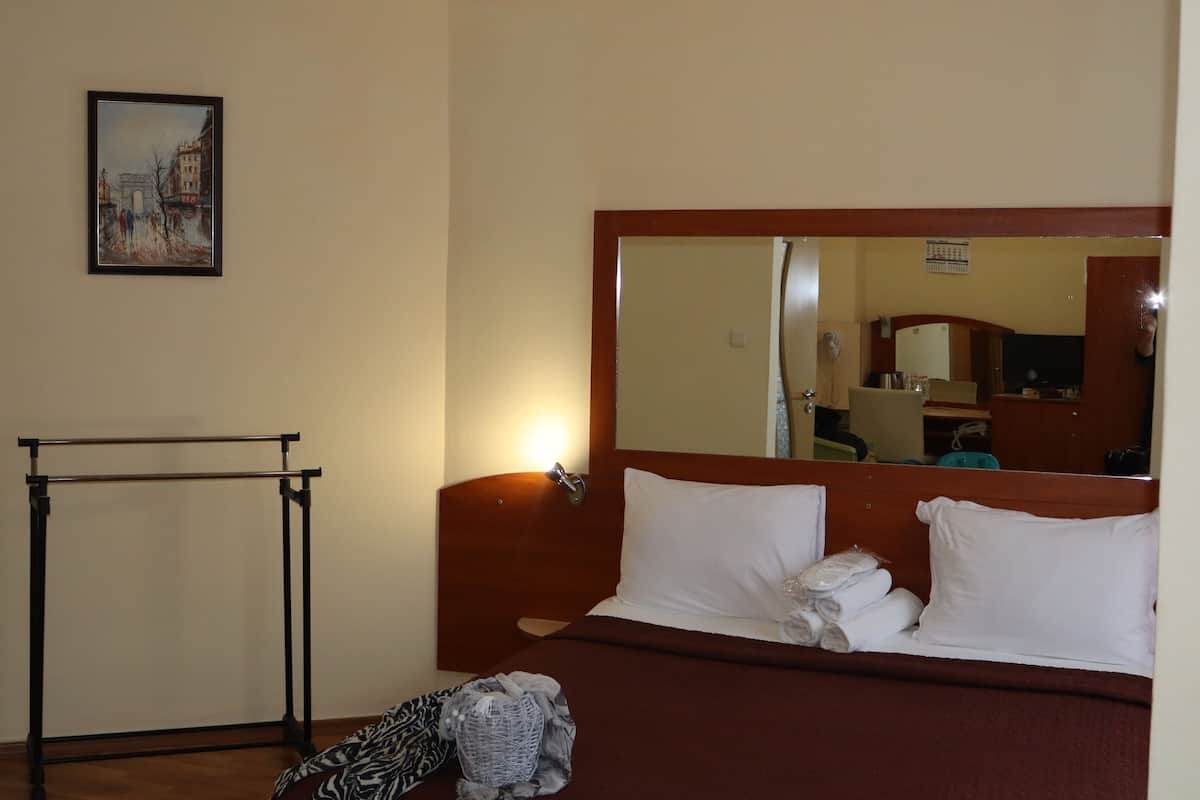 A hotel room with a bed, a wooden headboard, a mirror, a framed picture on the wall, and a small table with a towel.