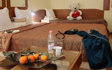 A neatly made bed with a teddy bear, a tray with fruits and a bottle of water, and a blue jacket on the side.