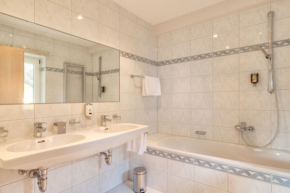 A bathroom with two sinks, a mirror, a bathtub, and a shower. - Hotel Nova (Gaschurn)