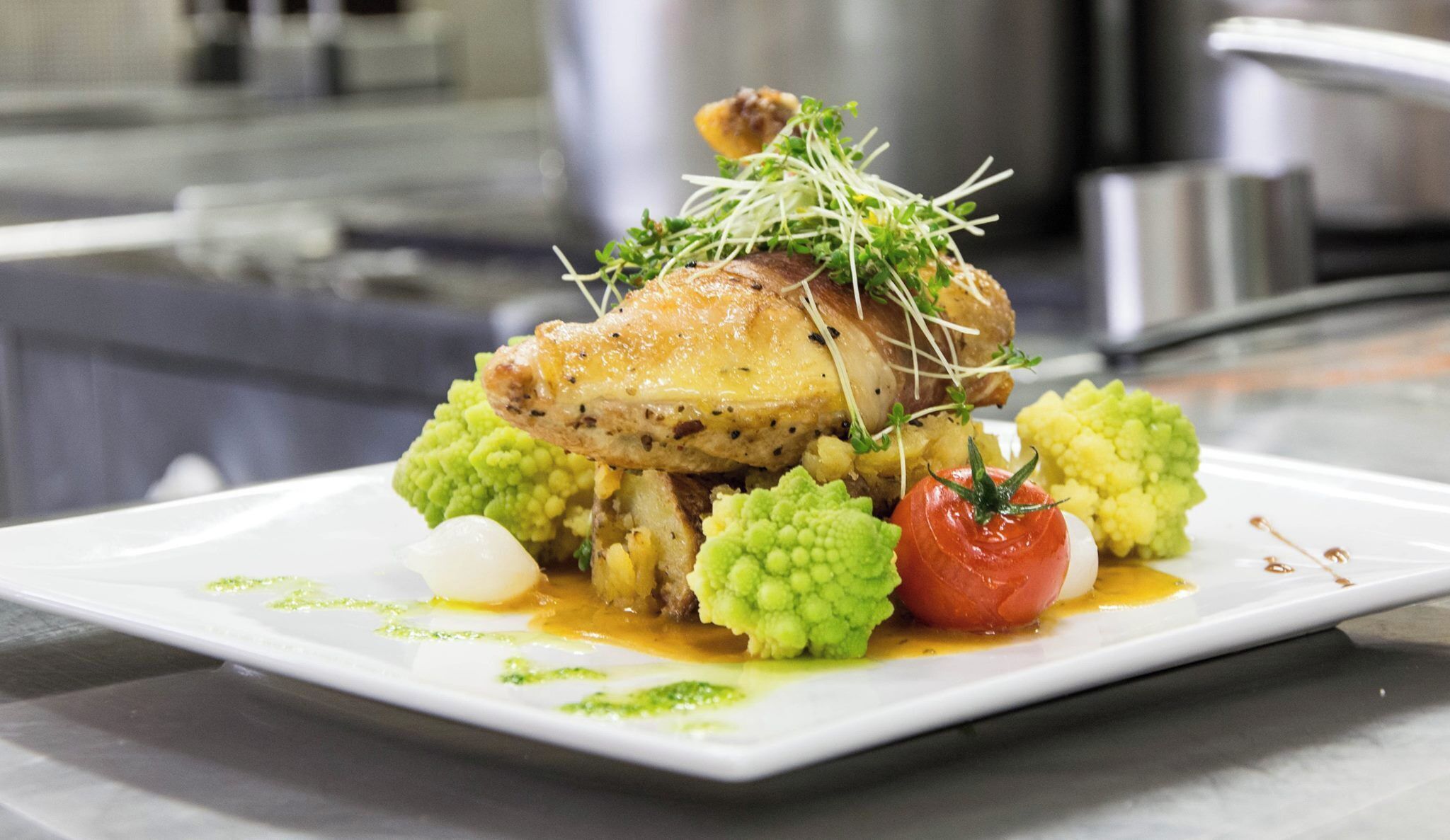 A plated dish with a roasted chicken, green vegetables, and a tomato garnish.