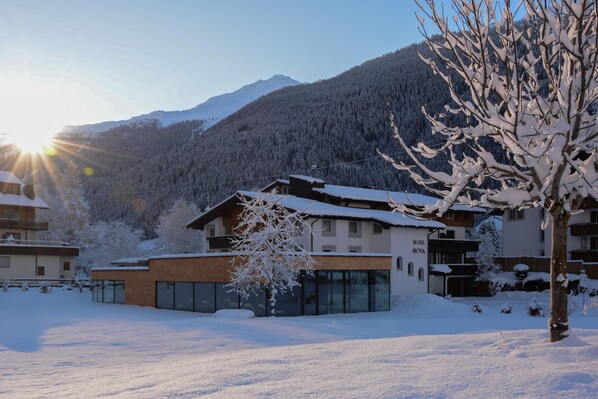A modern hotel with a glass facade, surrounded by snow-covered trees and mountains.