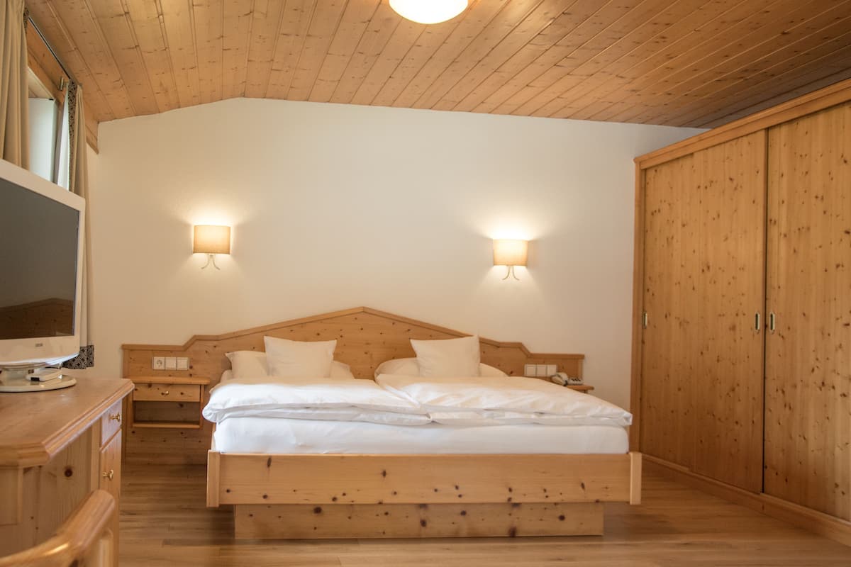 A wooden bed with white linens, two bedside tables, a wooden wardrobe, and two wall-mounted lights.
