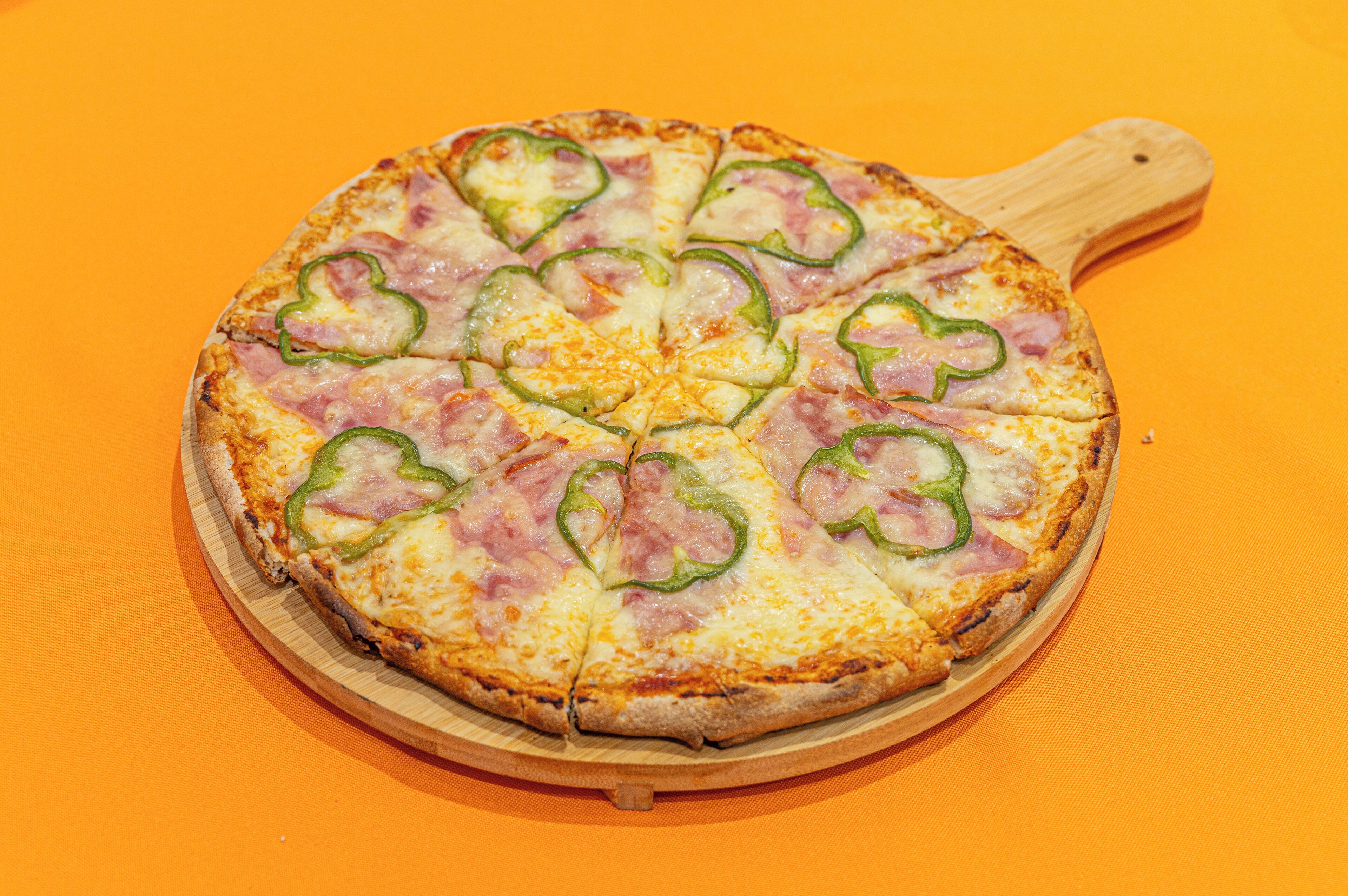 Pizza com fiambre e pimentões verdes sobre uma tábua de madeira.