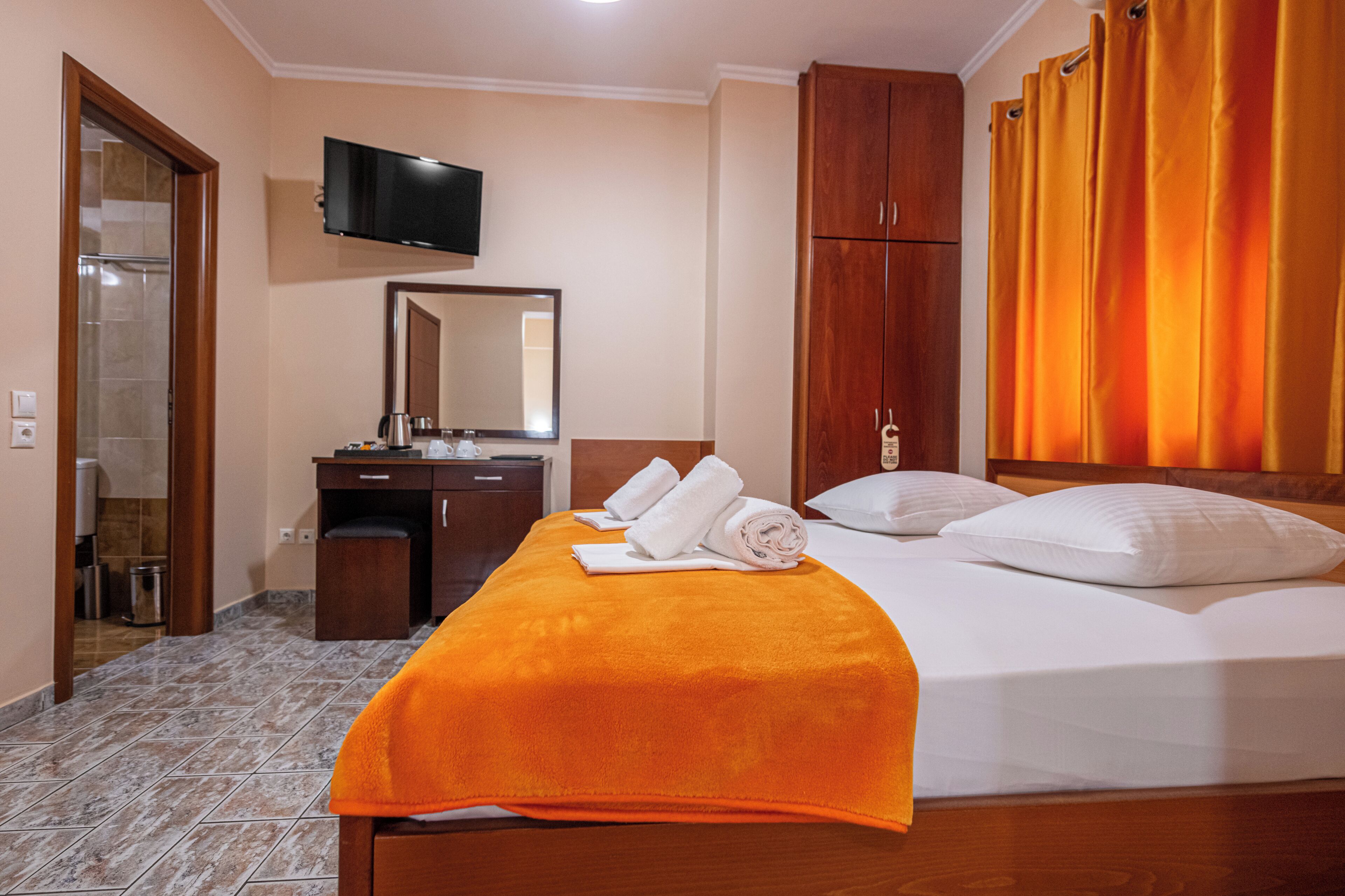 Ein Hotelzimmer mit einem Bett, einem Schreibtisch mit Spiegel, einem Fernseher und einem durch eine offene Tür einsehbaren Badezimmer.