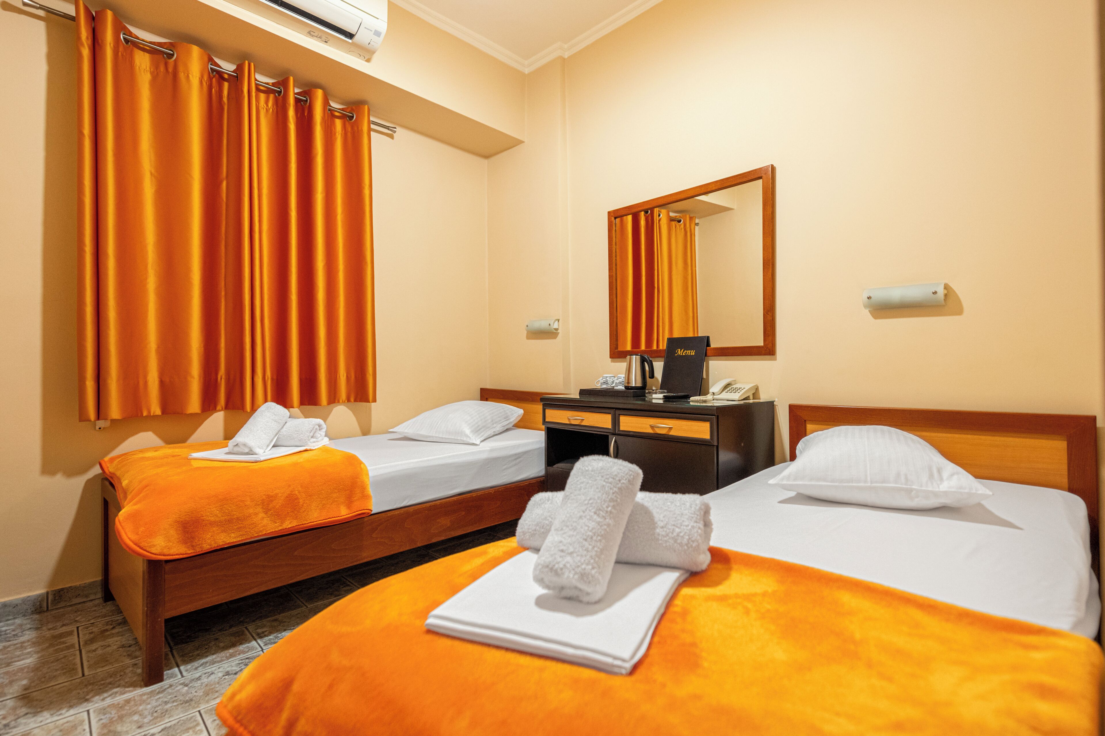 Habitación de hotel con dos camas, un aparador de madera, un espejo y un equipo de aire acondicionado.