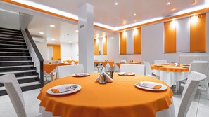 A modern dining area with round tables, white chairs, and orange tablecloths. - Faros 1 Hotel (Piraeus)