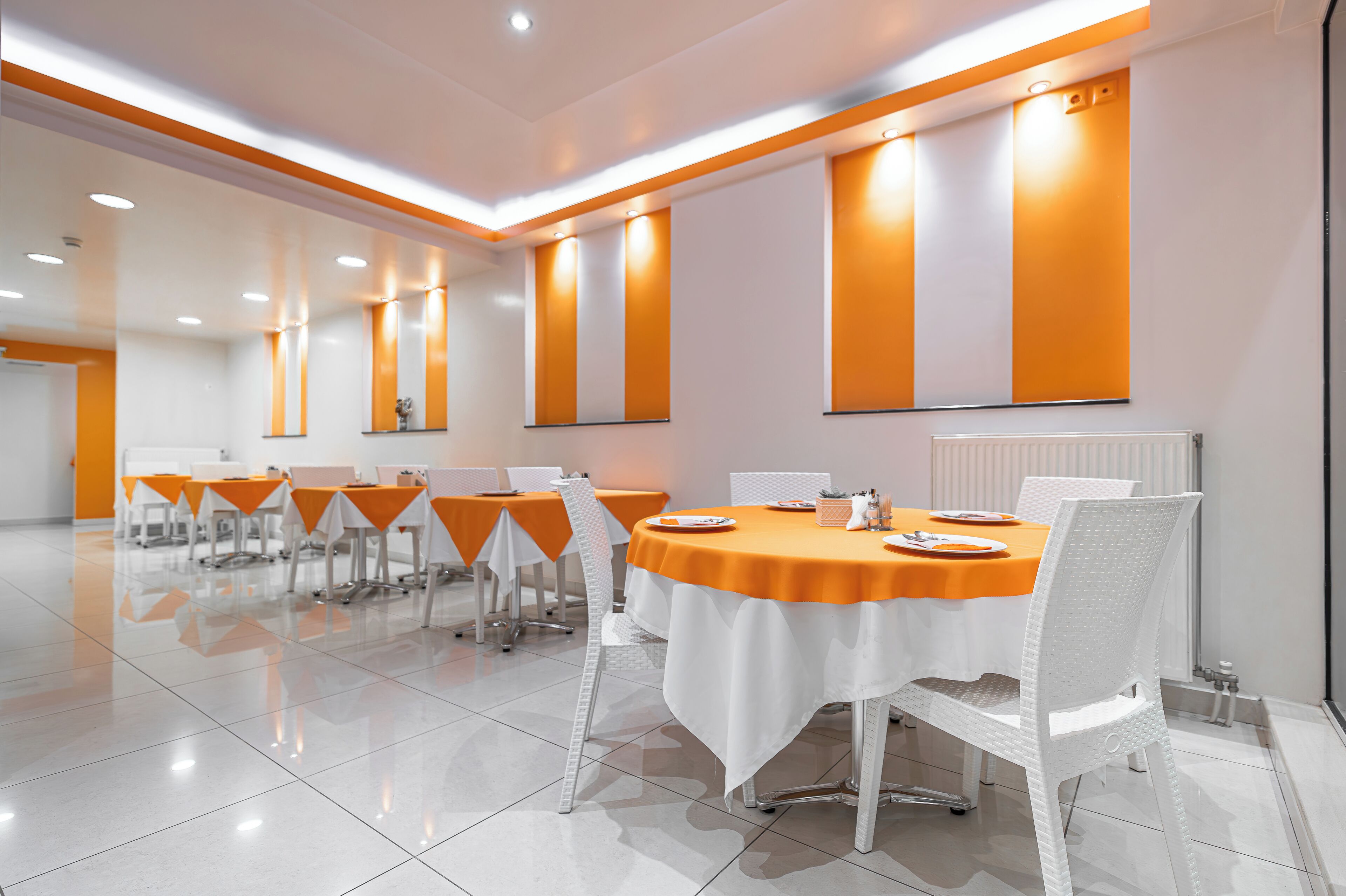 Un salón de conferencias con sillas y mesas blancas, manteles naranjas y una pizarra en la pared.
