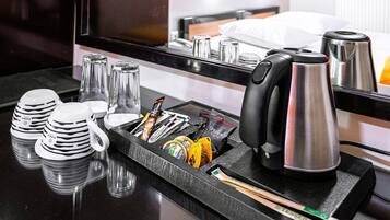A hotel kitchen counter with a coffee maker, tea kettle, and various utensils.