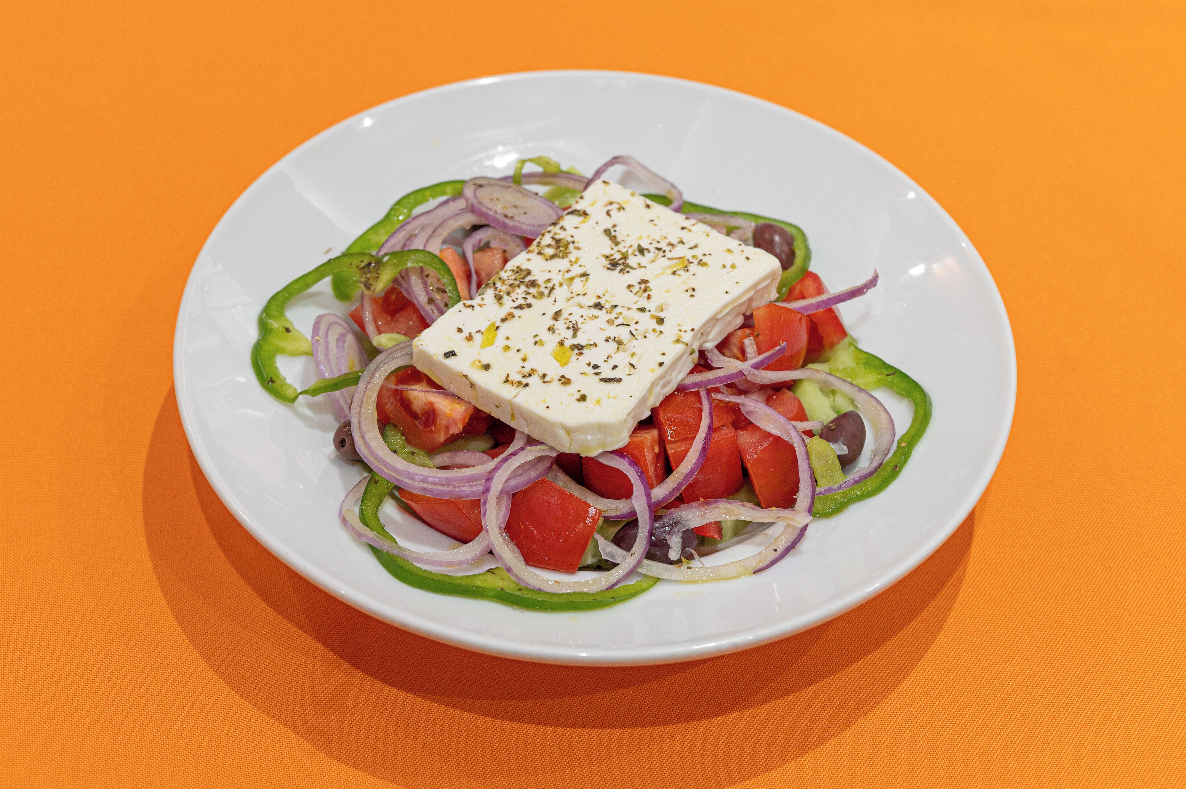 A plate of salad with feta cheese, tomatoes, cucumbers, and red onions on an orange tablecloth.