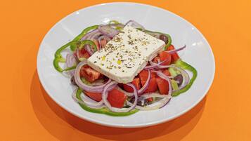 A plate of salad with feta cheese, tomatoes, cucumbers, and red onions on an orange tablecloth.