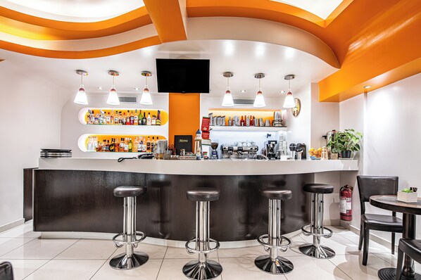 A modern bar area with a curved counter, multiple stools, a television above the bar, and a variety of bottles and bar tools. - Faros 1 Hotel (Piraeus)