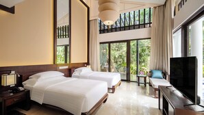 A hotel room with two beds, a TV, a desk, and a balcony with a view of greenery. - Banyan Tree Sanya (Sanya)