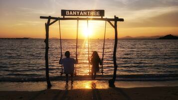 A swing set labeled "BANYANTREE" at a beach during sunset.