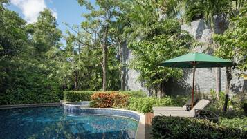 A swimming pool with a tiled edge, surrounded by lush greenery and a stone wall.