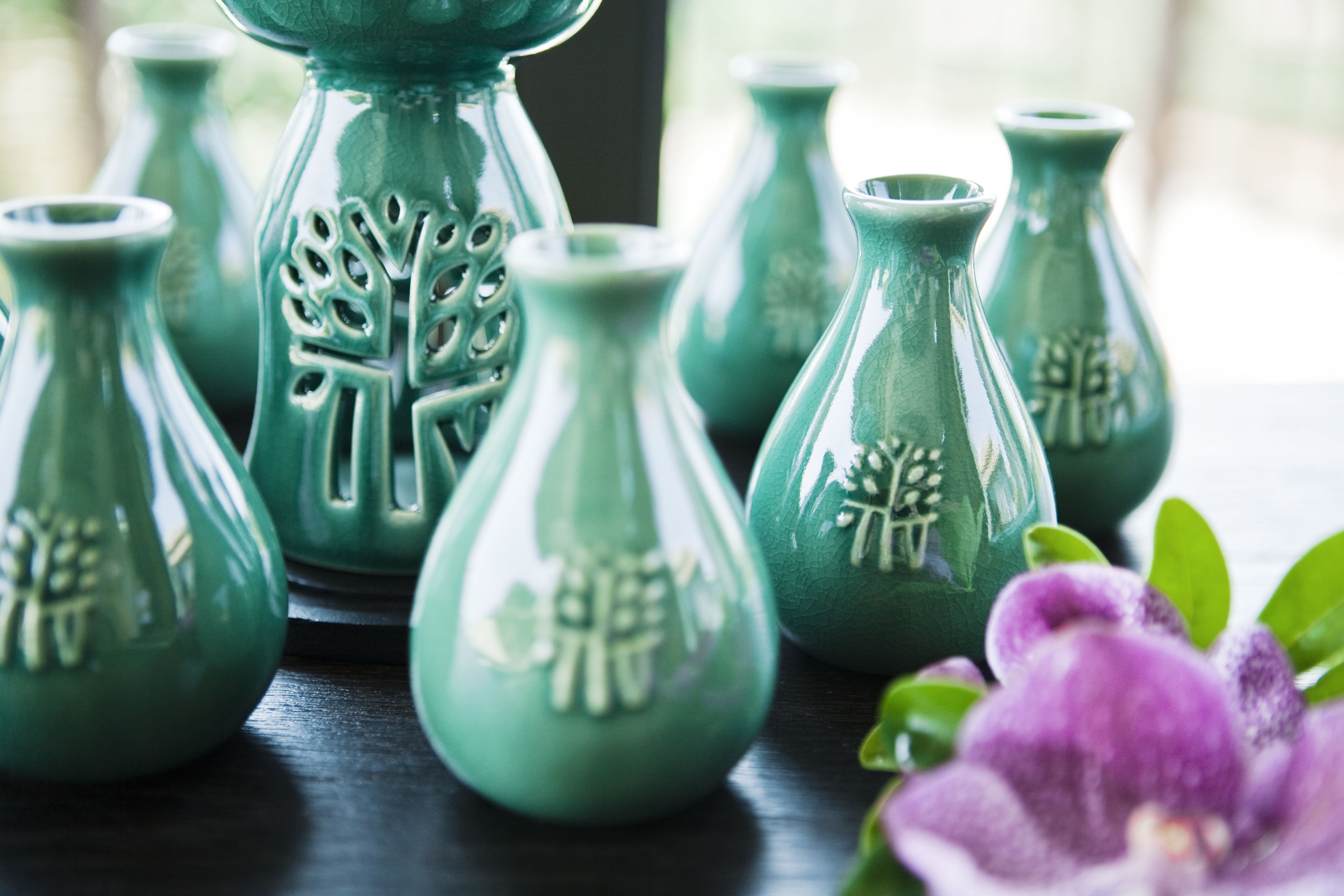A collection of green ceramic vases with embossed designs on a dark surface.