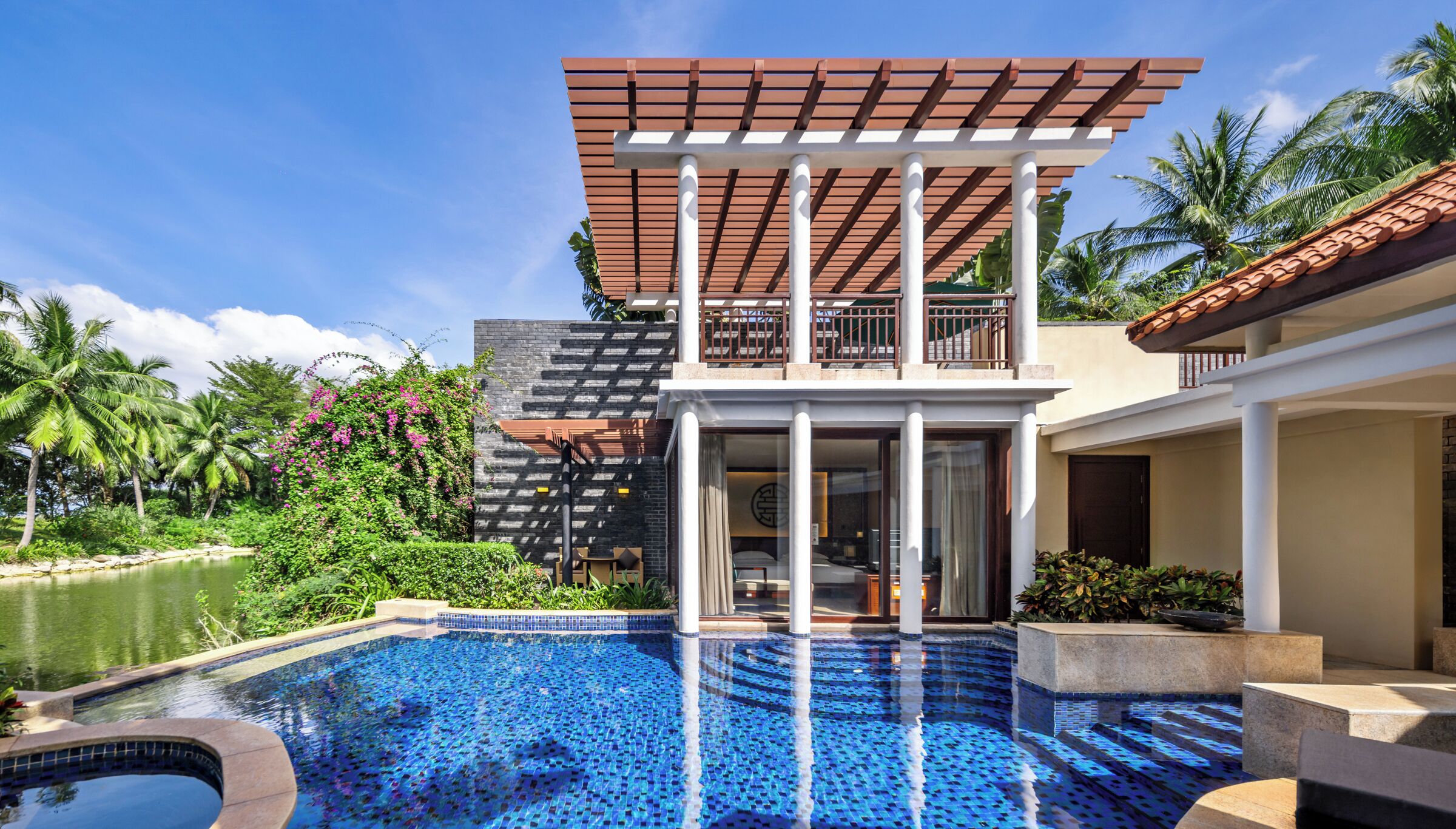 A modern hotel with a pool, a covered outdoor area, and lush greenery.