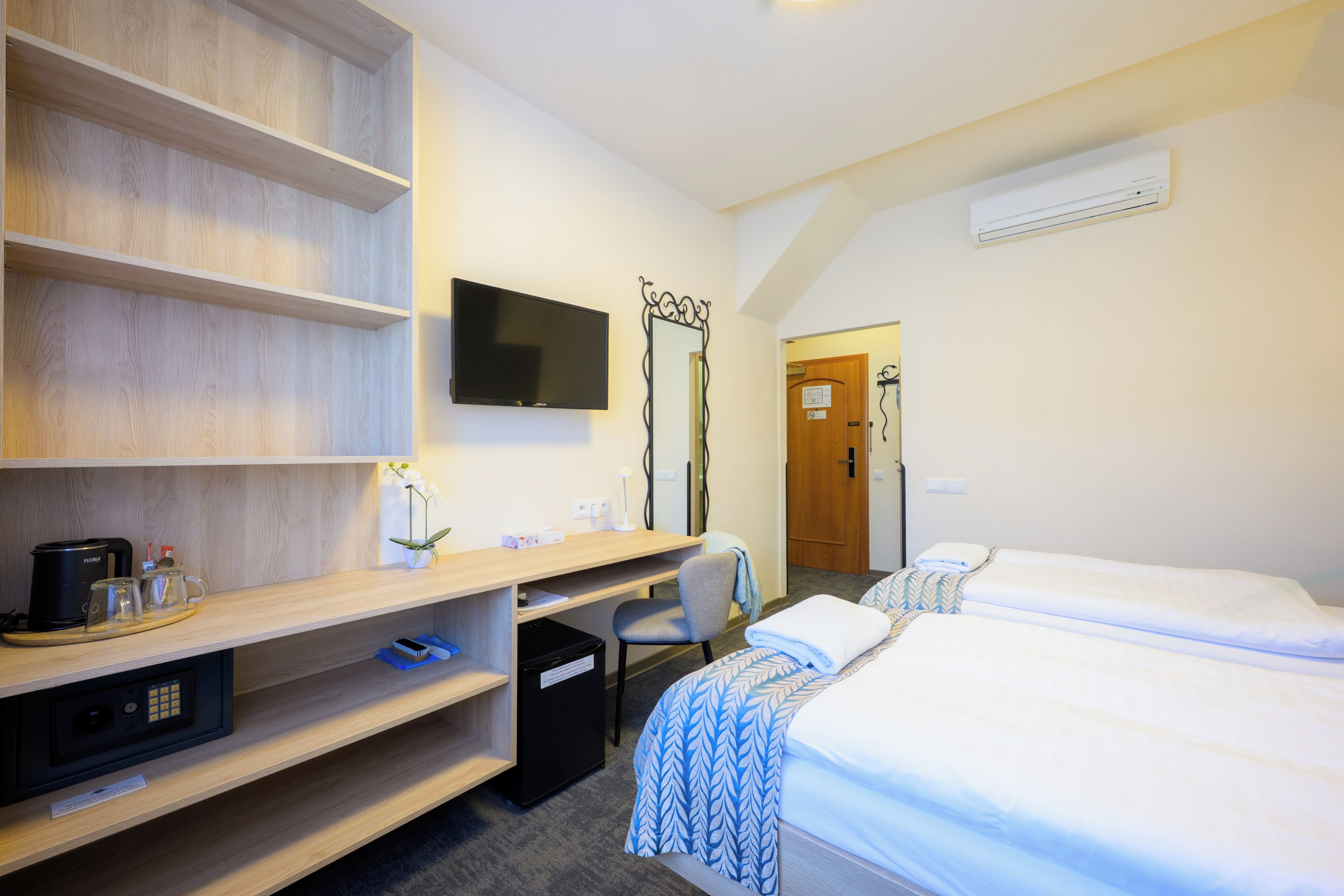 Habitación de hotel con cama, escritorio, silla, televisor y cesto de basura.