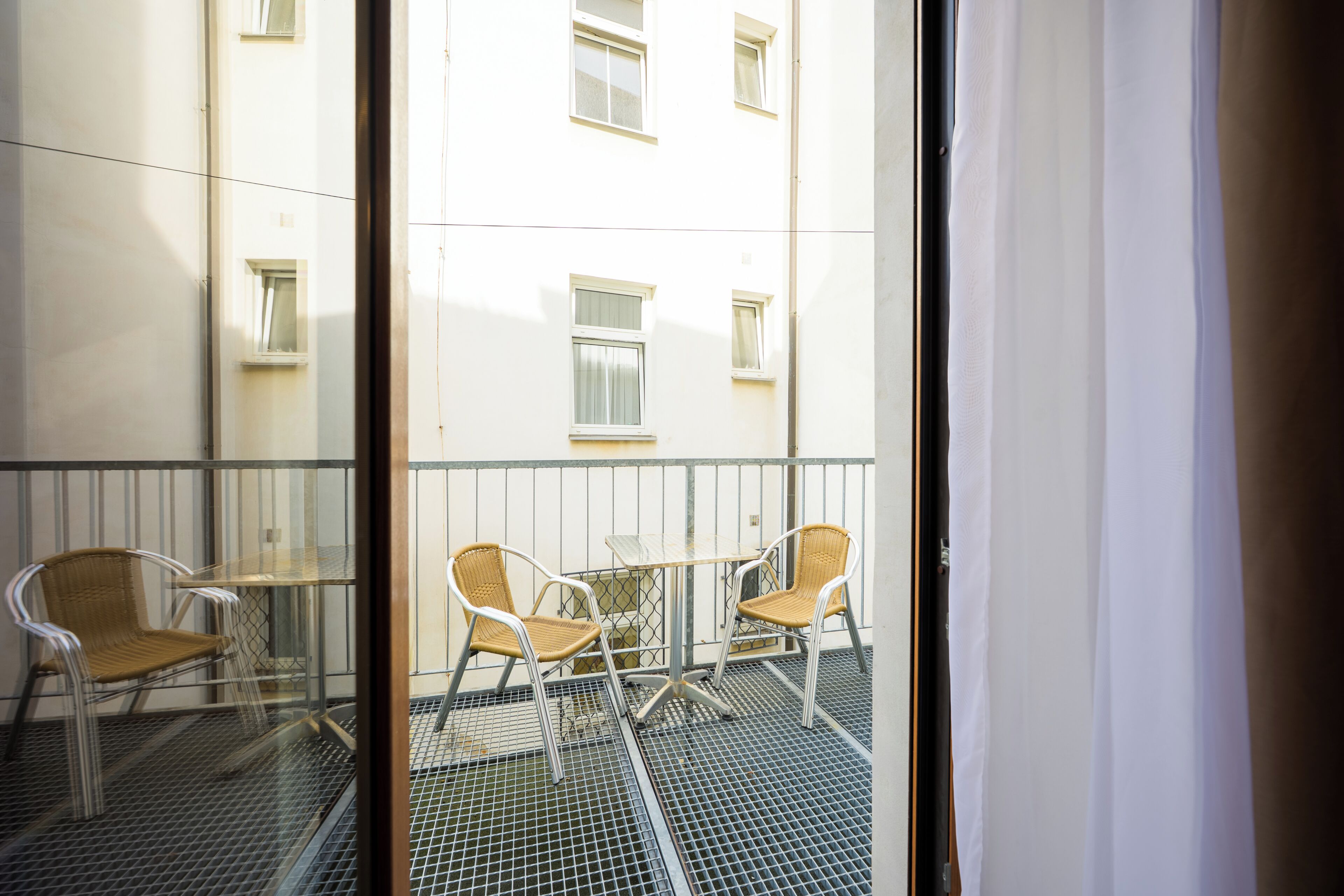 A balcony with two wicker chairs and a small table, overlooking a building with multiple windows.
