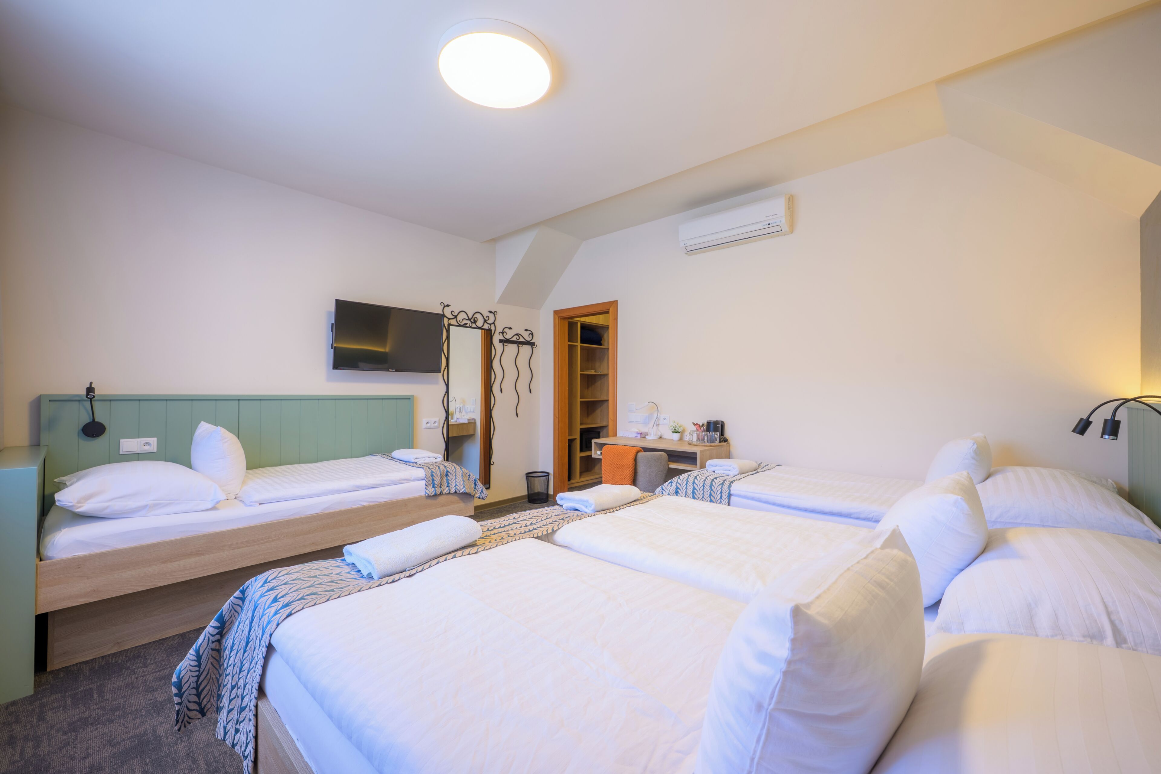 A hotel room with four single beds, a TV, a desk with a chair, and a wardrobe.