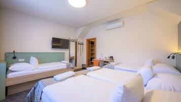 A hotel room with four single beds, a TV, a desk with a chair, and a wardrobe.