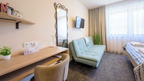 Une chambre d’hôtel avec un canapé, une télévision, un bureau avec une plante et un lit.