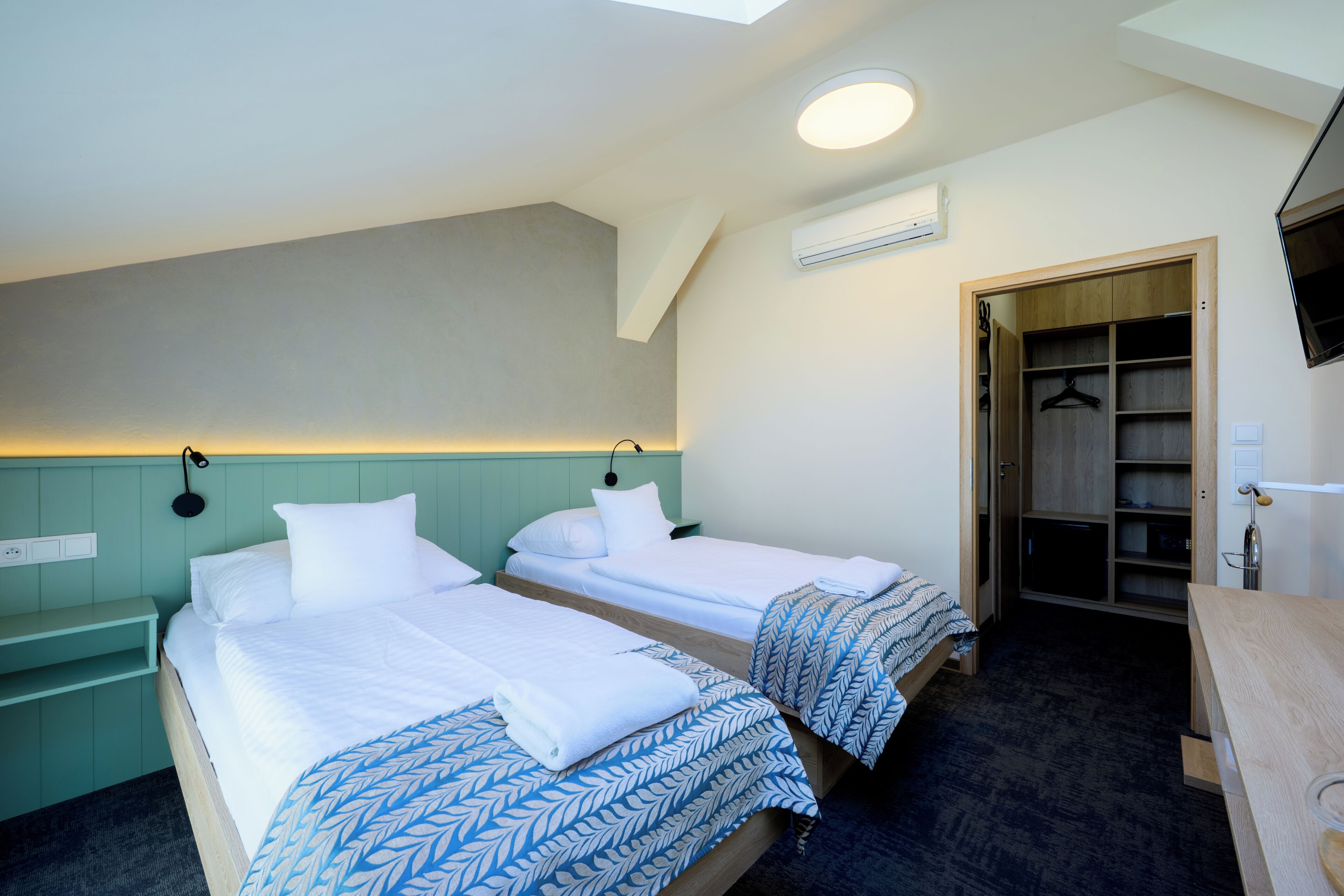A hotel room with two beds, a desk, a wardrobe, and a TV.