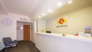 Un comptoir de réception d’hôtel avec une horloge, une enseigne indiquant « Hôtel », et une autre enseigne, « Recepce », placée au-dessus.