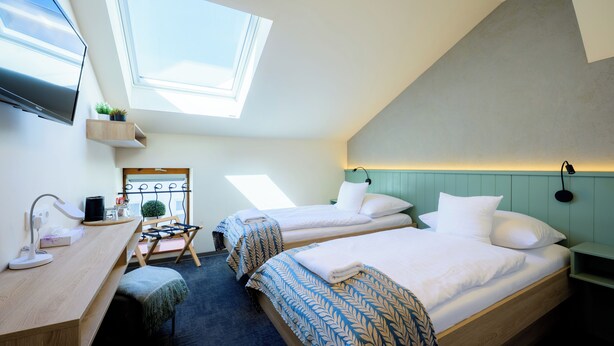 Une chambre d’hôtel moderne dotée d’une lucarne, de deux lits, d’un bureau avec un ordinateur et d’une télévision.