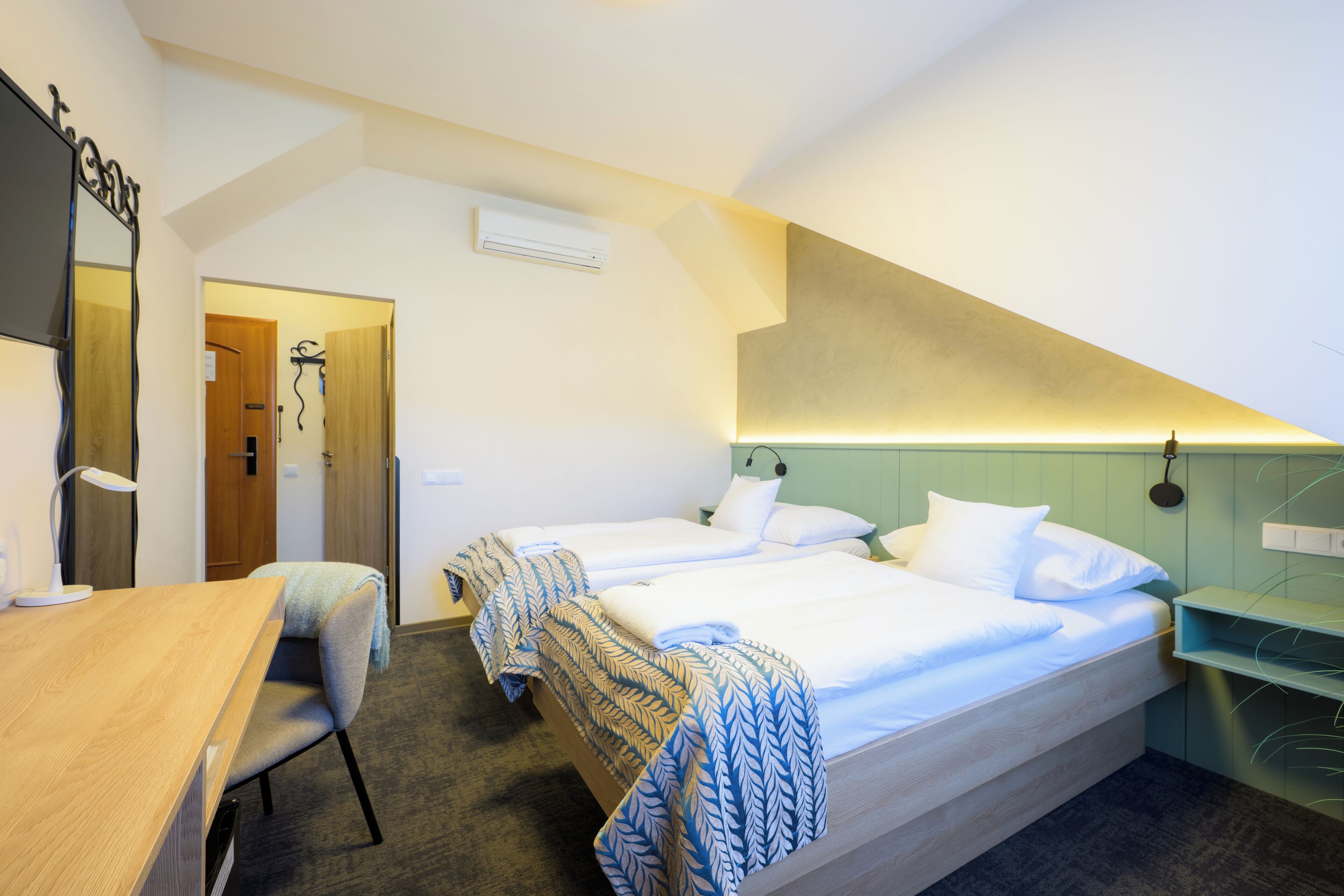 Habitación de hotel con dos camas, un escritorio, una silla, un espejo y un estante en la pared.
