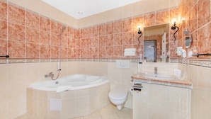 A bathroom with a bathtub, toilet, and sink, featuring marble tiles and a large mirror. - Hotel Palace (Plzen)