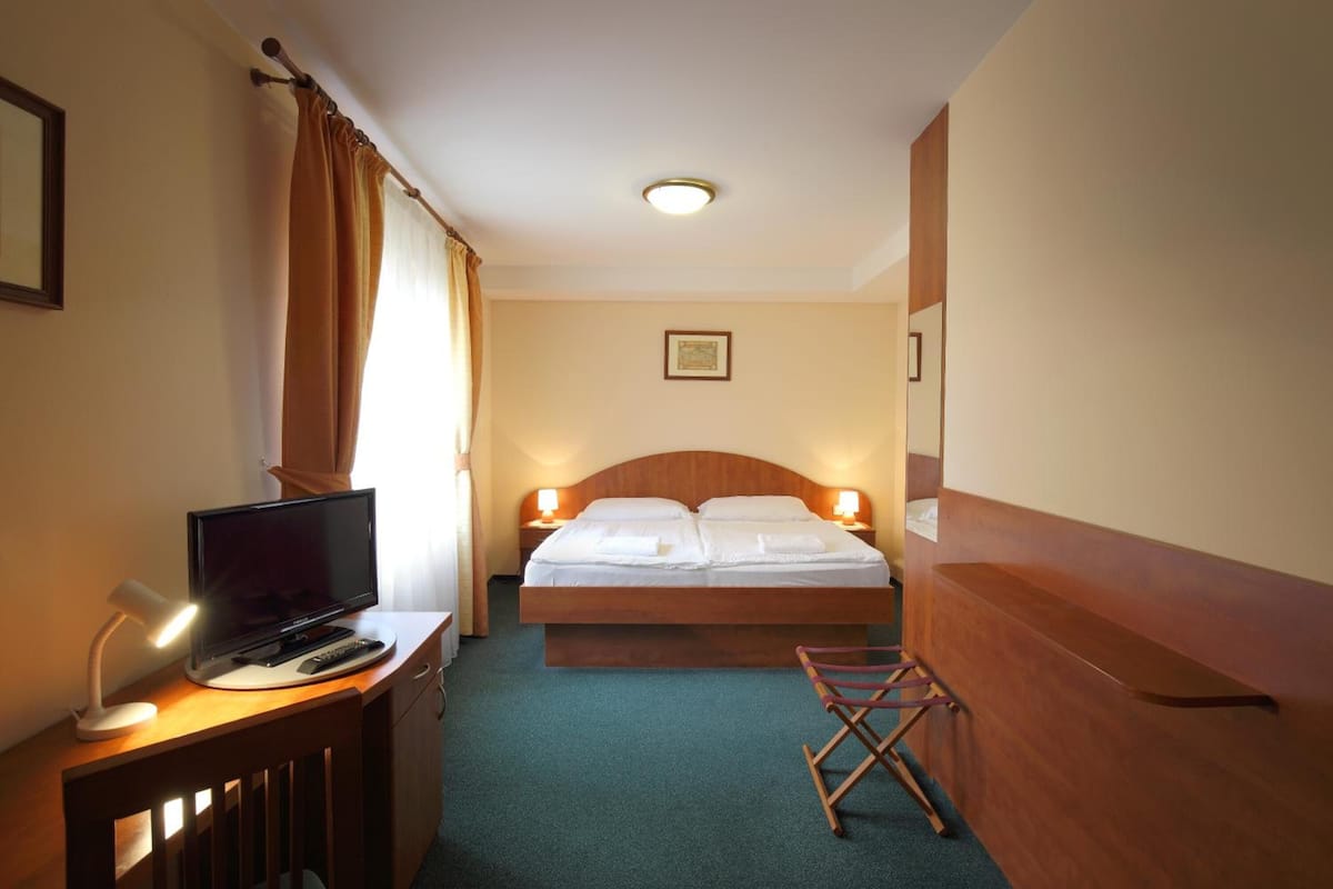 A hotel room with a bed, bedside lamps, a desk with a TV, and a chair.