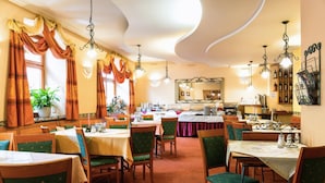 A dining area with multiple tables and chairs, a kitchen in the background, and a large mirror on the wall. - Hotel Palace (Plzen)