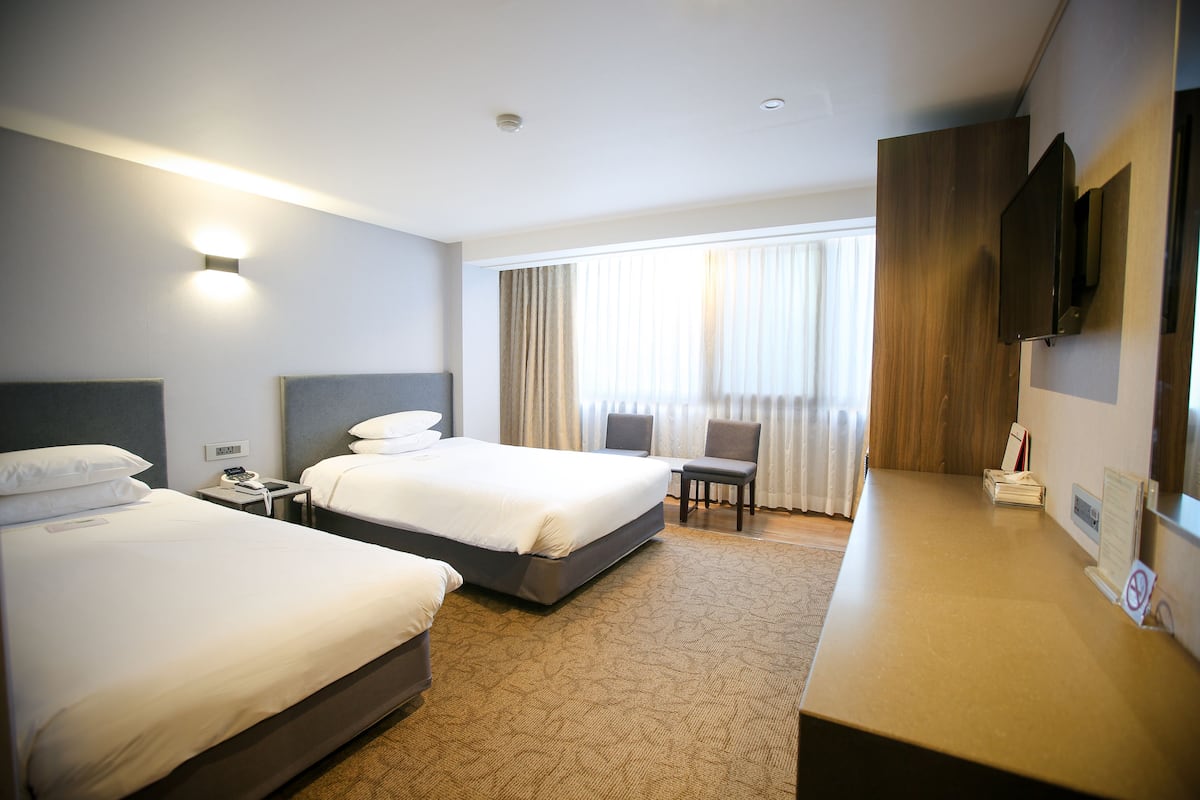 A hotel room with two beds, a desk, a chair, a TV, and a window with curtains.