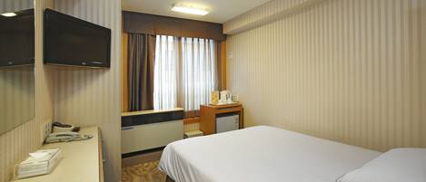 Habitación de hotel con cama, escritorio con teléfono, televisión de pantalla plana, pequeño escritorio con cafetera y ventana con cortinas.