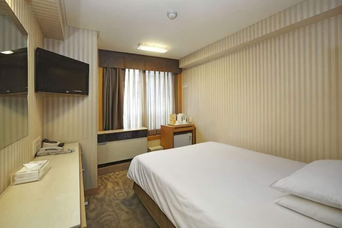 A hotel room with a bed, a desk with a telephone, a television mounted on the wall, and a window with curtains.