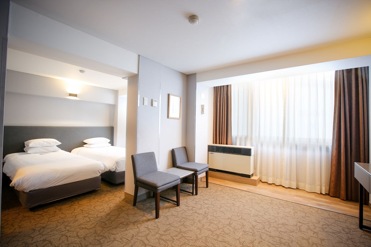 A hotel room with two beds, a desk, and a chair.