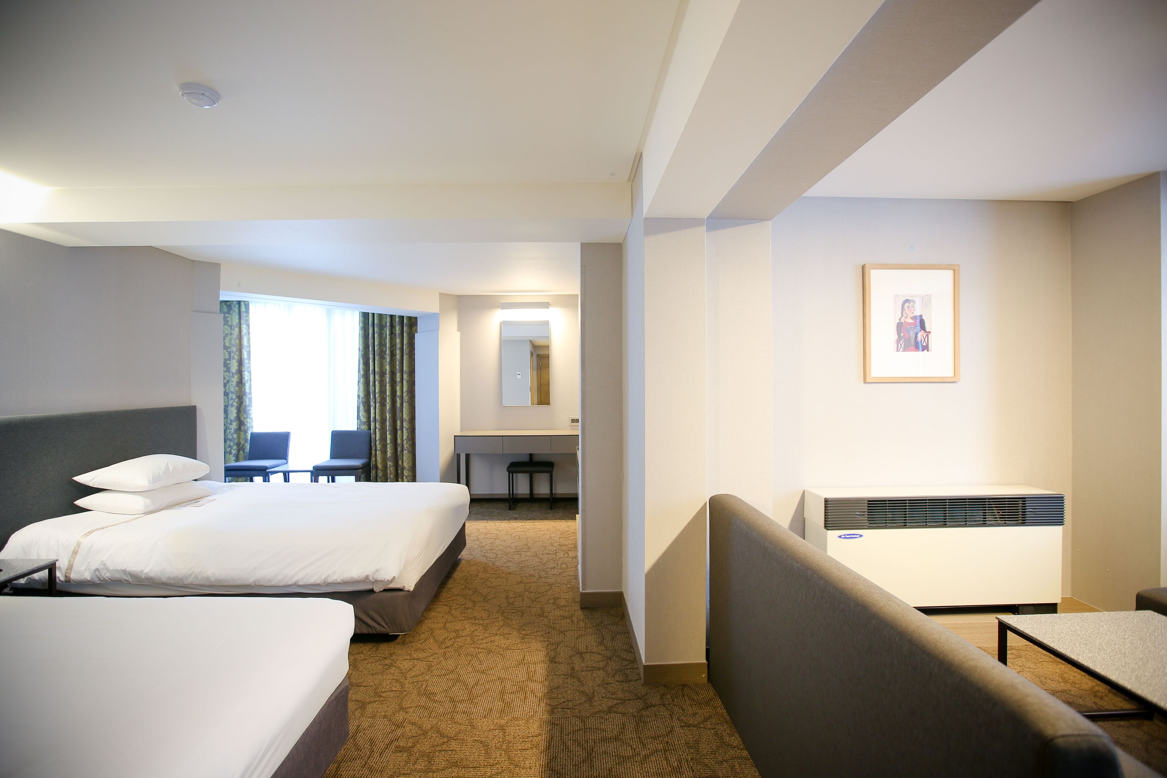 A hotel room with two beds, a desk, a chair, a framed picture on the wall, and an air conditioning unit.