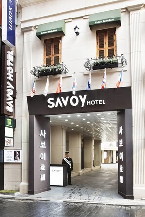 The entrance to Savoy Hotel with a signboard, a doorman, and flags. - Savoy Hotel (Seoul)