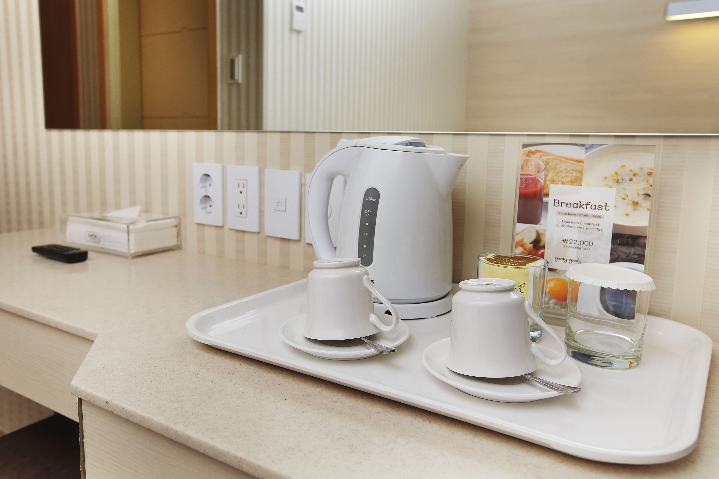 Bandeja de desayuno con cafetera, tazas y un menú en una habitación de hotel.