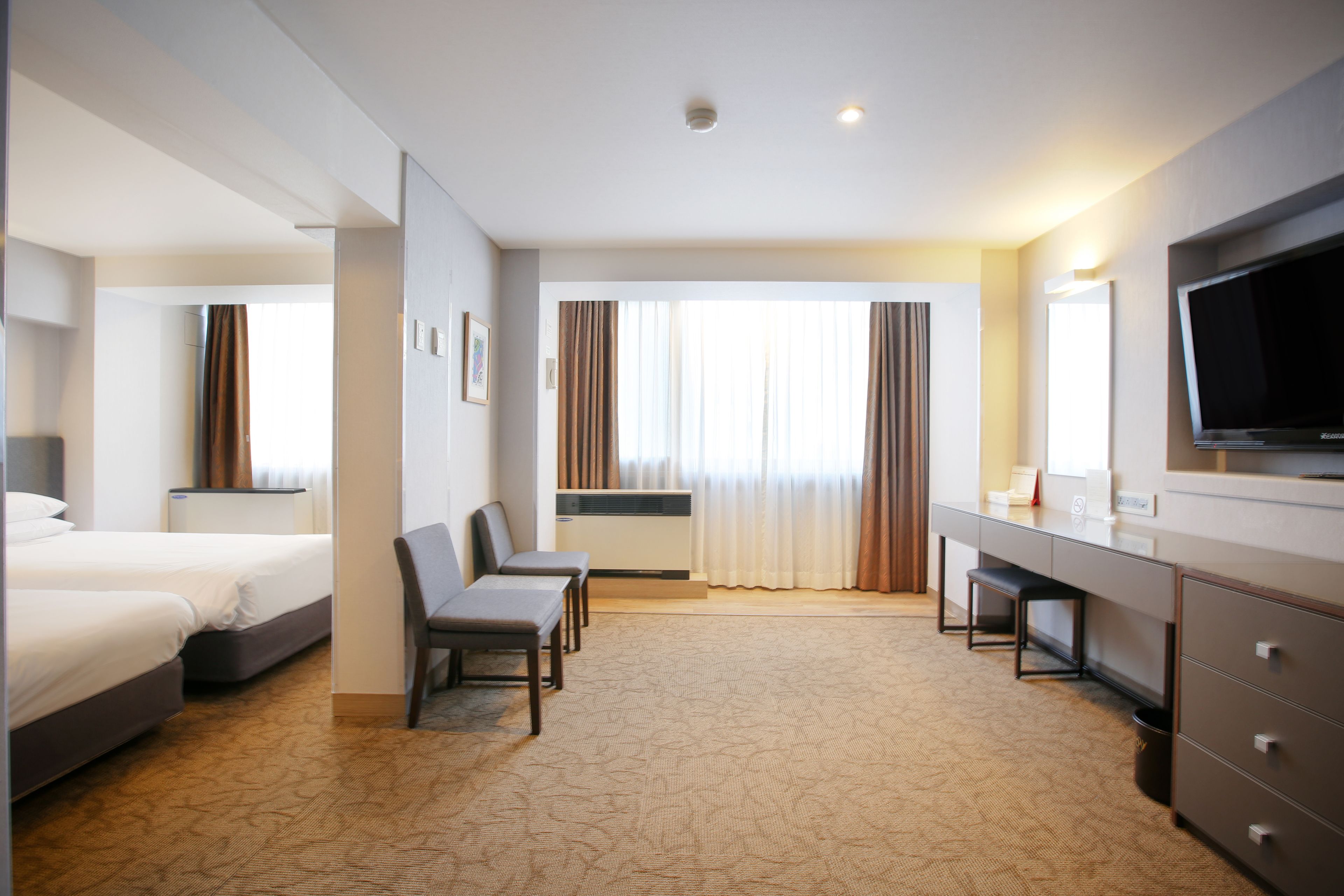 Une chambre d’hôtel avec deux lits, un bureau, une chaise, une télévision et une grande fenêtre avec des rideaux.