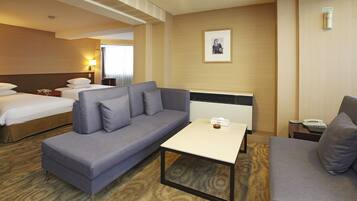 A hotel room with a large bed, a sofa, a small table, and a bedside table with a lamp.