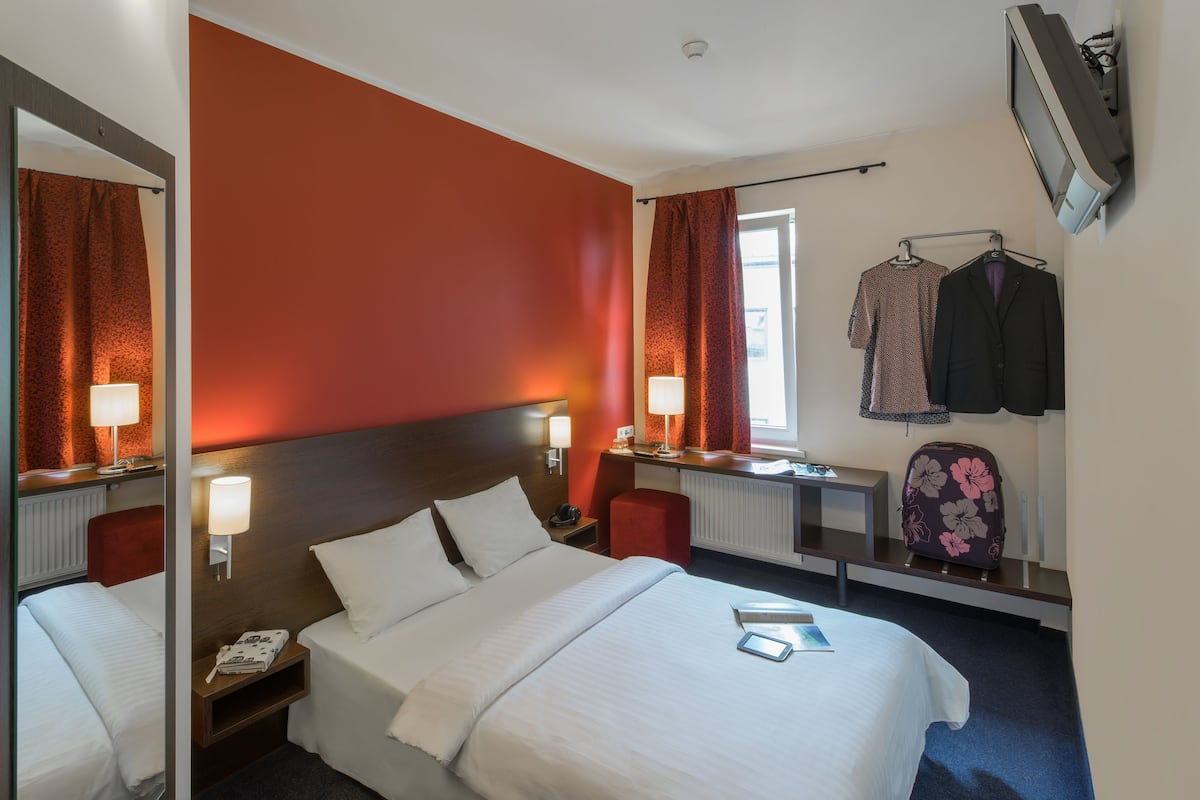 A hotel room with a large bed, two bedside tables, a desk, a chair, a mirror, and a window with curtains.