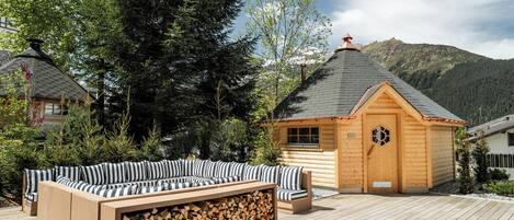 Eine Holzhütte mit geneigtem Dach, einer eingebauten Holzbank mit gestreiften Kissen und einem Holzstapel.