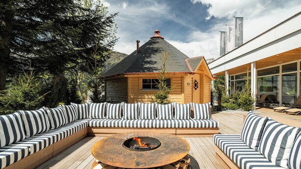 Une cabane en bois avec un foyer au centre, entourée de sièges d’extérieur à rayures.