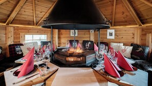 L’intérieur chaleureux d’un chalet avec un poêle à bois central, des murs en bois et un plafond haut.